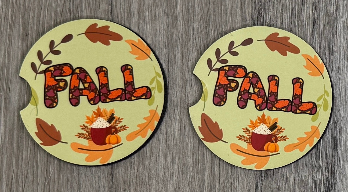 Two round fall-themed coasters with 'FALL' text and leaf designs on a wooden surface.